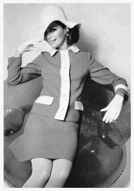 Modella seduta con cappello e guanti bianchi che indossa un tailleur Hettemarks modello Amour in crêpe di pura lana con riporti bianchi.