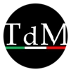 Un logo circolare nero con al centro le lettere “T d M” in bianco, sormontate da una sottile linea orizzontale tricolore (verde, bianco e rosso) posta sotto le lettere.